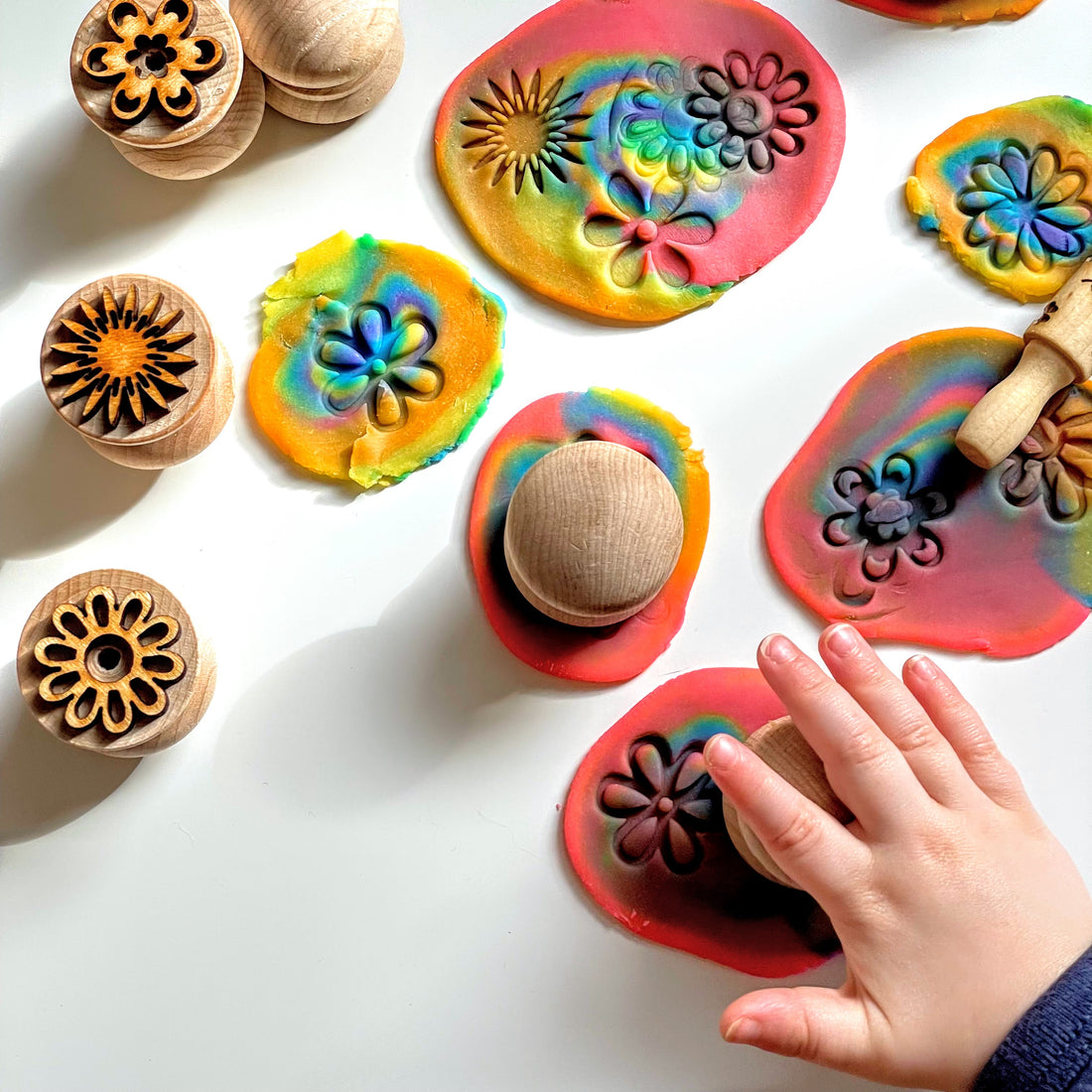 Toddler hand using a playdough stamp to create flower patterns in rainbow colored playdough
